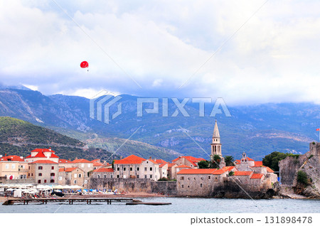 Picturesque view of old town, Adriatic sea and tourists on a parachute, Budva, Montenegro. Topic of summer vacation, travel, leisure for adventure tourist. Popular tourist pastime with parascending Picturesque view of old town, Adriatic sea and tourists on a parachute, Budva, Montenegro. Topic of summer vacation, travel, leisure for adventure tourist. Popular tourist pastime with parascending 131898478