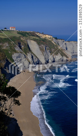 A breathtaking wide shot of the rugged coastline in Gijon, Asturias, Spain, featuring steep, layered cliffs covered with rich greenery 131898529