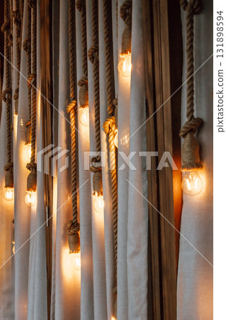 decorative lighting design featuring warm bulbs hanging from ropes against soft fabric backdrop. decorative lighting design featuring warm bulbs hanging from ropes against soft fabric backdrop. 131898594