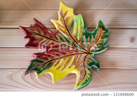 clay dish in shape maple leaf crafted in vibrant autumn colors on wooden table. closeup. clay dish in shape maple leaf crafted in vibrant autumn colors on wooden table. closeup. 131898600