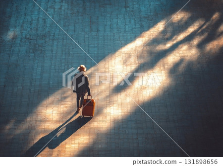 Person traveling with luggage walking through sunlight and shadows 131898656