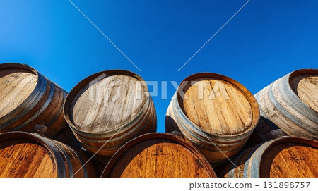Wooden barrels against a clear blue sky. Stacked and aging, they evoke tradition and craftsmanship. A picturesque scene of winemaking heritage. 131898757
