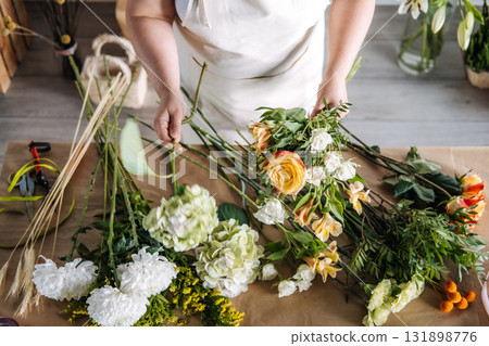 Woman assembling a bouquet with yellow rose and greenery in a seasonal floristry setting. Mindful crafting, slow floristry, bouquet making workshop, creative floral hobby 131898776