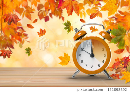 Orange alarm clock placed on a wooden surface with falling leaves 131898892