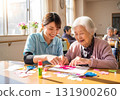 這是日託中心的場景，護理人員和老年婦女一邊微笑一邊享受手工藝的樂趣。 131900260