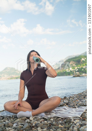 Sporty woman on the seaside enjoying peaceful moment after workout and drinking fresh water. 131901097