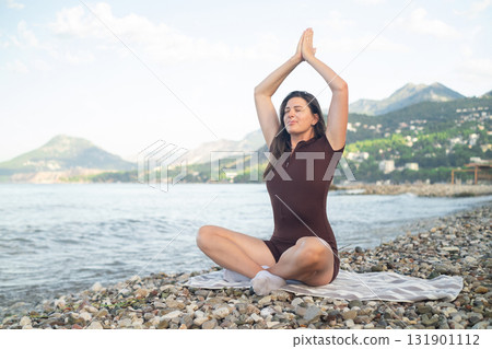 Relaxation and harmony woman doing yoga on sand with sea and sun in the background peaceful outdoor scene Relaxation and harmony woman doing yoga on sand with sea and sun in the background peaceful outdoor scene 131901112