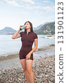 Woman restoring energy after workout by the sea fitness and health drinking water on the beach outdoor wellness 131901123