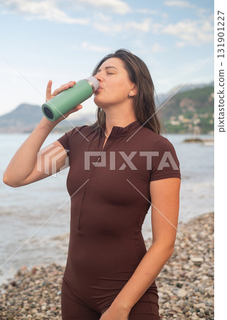 Woman in sportswear relaxing after morning workout by the sea drinking water from bottle outdoor fitness scene Woman in sportswear relaxing after morning workout by the sea drinking water from bottle outdoor fitness scene 131901227