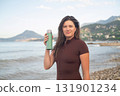 Healthy morning by the ocean. Sporty woman hydrating and relaxing after exercise. 131901234