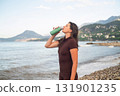 Morning fitness by the sea. Woman recharging energy and drinking water after workout. 131901235