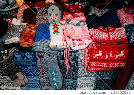 Traditional Christmas Winter Market Trading Houses With Warm Clothes, Wear And Hats. Colorful Knitted Traditional European Warm Clothes - Mittens and Scarfs. Xmas Souvenir From Europe. Traditional Christmas Winter Market Trading Houses With Warm Clothes, Wear And Hats. Colorful Knitted Traditional European Warm Clothes - Mittens and Scarfs. Xmas Souvenir From Europe. 131902923