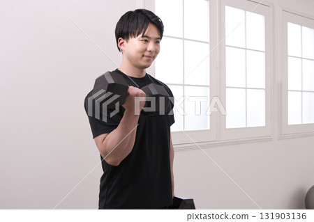 一名 20 多歲的男子正在用啞鈴進行肌肉訓練 一名 20 多歲的男子正在用啞鈴進行肌肉訓練 131903136