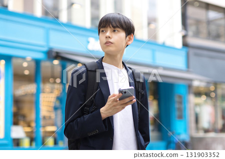 A male businessman in his twenties standing in the street with a smartphone A male businessman in his twenties standing in the street with a smartphone 131903352