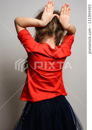 Girl in red shirt and dark skirt makes bunny ears behind her head. Girl in red shirt and dark skirt makes bunny ears behind her head. 131904465