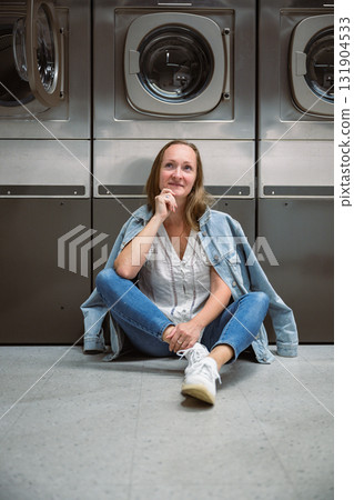 Woman sitting on floor in self service laundromat while waiting laundry 131904533