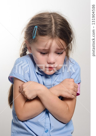 A young girl with a sad expression, arms crossed, looking down. 131904586