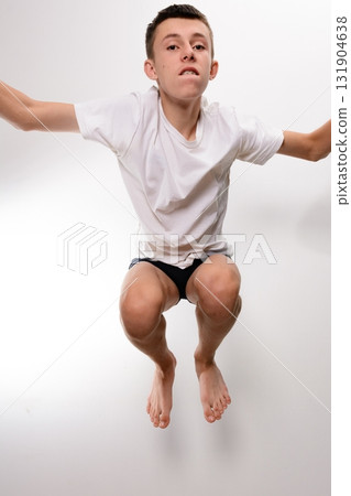Teenager mid-jump, arms outstretched, wearing a white shirt and dark shorts against a white background. 131904638