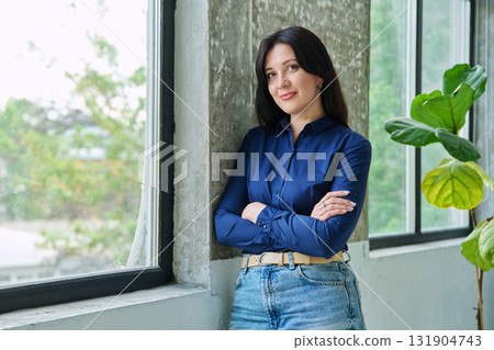 Portrait of beautiful confident woman looking at camera with crossed arms, near window Portrait of beautiful confident woman looking at camera with crossed arms, near window 131904743