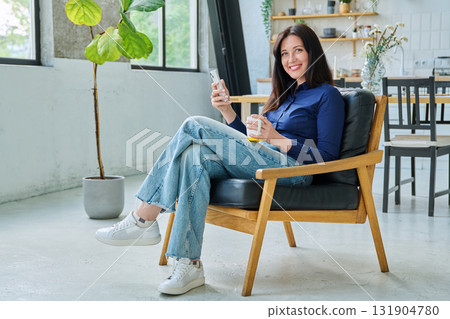 Young happy woman sitting at home in chair using a smartphone Young happy woman sitting at home in chair using a smartphone 131904780