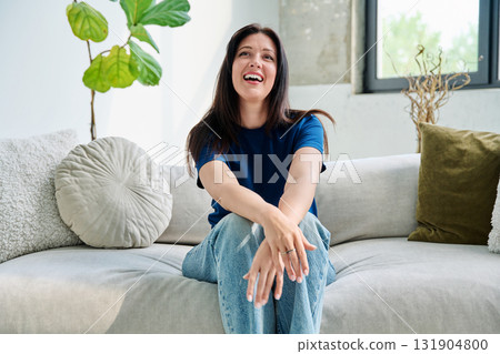 Portrait of beautiful smiling brunette woman sitting on sofa in living room Portrait of beautiful smiling brunette woman sitting on sofa in living room 131904800
