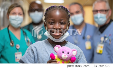 Hopeful Child with Teddy Bear, supported by medical team, radiating joy in hospital setting. Symbolizing resilience and care during health challenges. 131904820