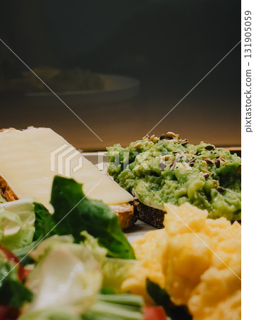 Wholemeal bread toasts with mashed avocado and cheese, scrambled eggs and fresh salad with lettuce, spinach, radish and tomato compose healthy breakfast or brunch. Nutritious morning meal. Good diet 131905059