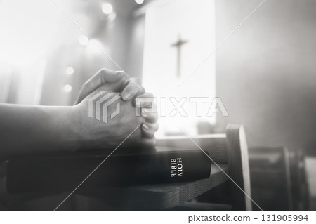 A believer praying with both hands together during a church service, with the Holy Bible and the cross of Jesus Christ in the background. A believer praying with both hands together during a church service, with the Holy Bible and the cross of Jesus Christ in the background. 131905994