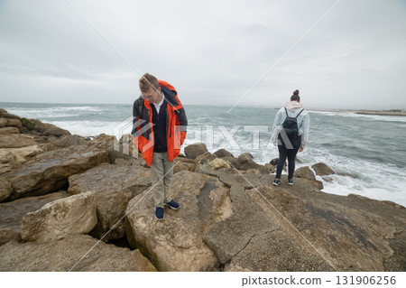 Young couple exploring rugged coast with crashing waves Young couple exploring rugged coast with crashing waves 131906256
