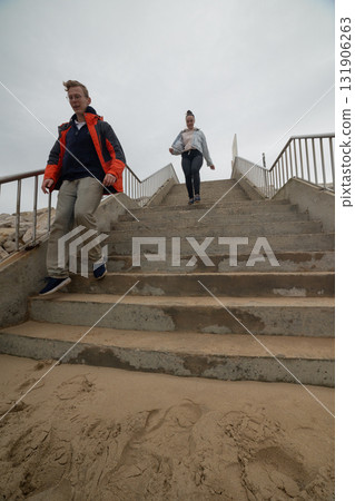Young couple descending concrete stairs to sandy beach Young couple descending concrete stairs to sandy beach 131906263