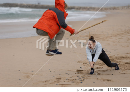 Young people playing imaginative stick fighting game on beach Young people playing imaginative stick fighting game on beach 131906273