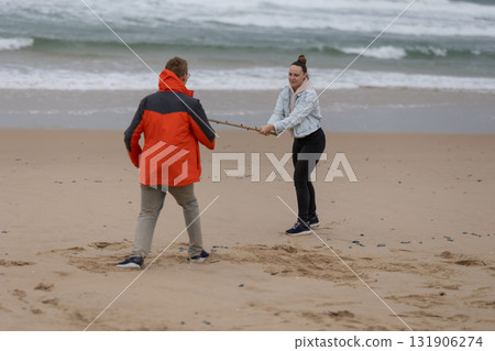 Couple battling over a stick on sandy ocean beach 131906274