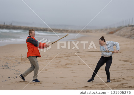 Man and woman playing stick fight battle on beach Man and woman playing stick fight battle on beach 131906276