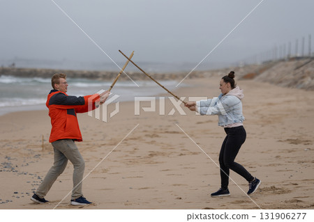 Couple playing sword fighting game on sandy beach Couple playing sword fighting game on sandy beach 131906277
