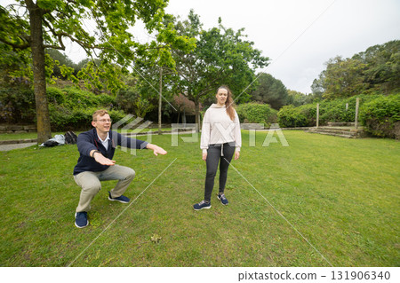 Man performing squat exercise with woman in park 131906340