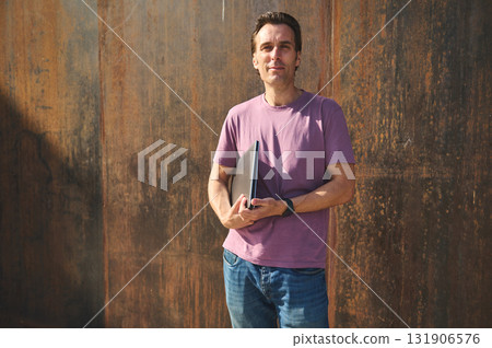 Casual Man With Notebook Standing Against Rusty Wall in Bold Portrait Casual Man With Notebook Standing Against Rusty Wall in Bold Portrait 131906576
