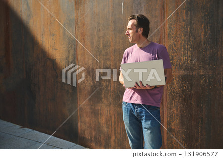 Professional Man With Laptop Standing Against Rusty Wall, Outdoor Tech Use Professional Man With Laptop Standing Against Rusty Wall, Outdoor Tech Use 131906577