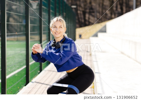 Young sportswoman performing squats with elastic band outdoors 131906652