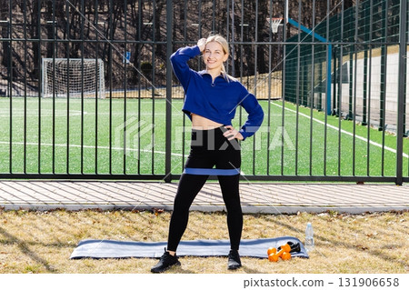 Confident sportswoman posing with resistance band on a sports field 131906658