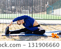 Young woman stretching on yoga mat, enjoying outdoor workout near sports field 131906660