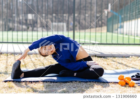 Young woman stretching on yoga mat, enjoying outdoor workout near sports field 131906660