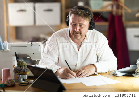 Positive middle-aged male dressmaker drawing on paper watching video-course 131906711