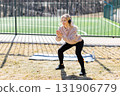 Young woman wearing headphones performing squats outdoors 131906779