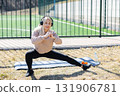 Young woman stretching legs and listening music with headphones during outdoor workout 131906781