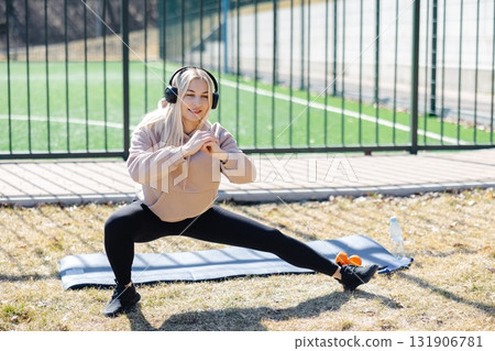 Young woman stretching legs and listening music with headphones during outdoor workout 131906781