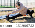 Young woman stretching outdoor wearing headphones and sportswear 131906782