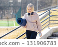 Young sporty woman carrying yoga mat and water bottle walking up the stairs 131906783