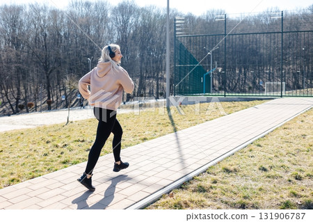 Young sportswoman running in the park listening music with headphones Young sportswoman running in the park listening music with headphones 131906787