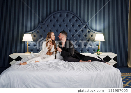 A man and a woman in silk pajamas with champagne are lying on a bed. A man and a woman in silk pajamas with champagne are lying on a bed. 131907005