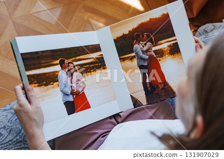 woman is holding and flipping through a photo book with a pregnancy photo shoot 131907029